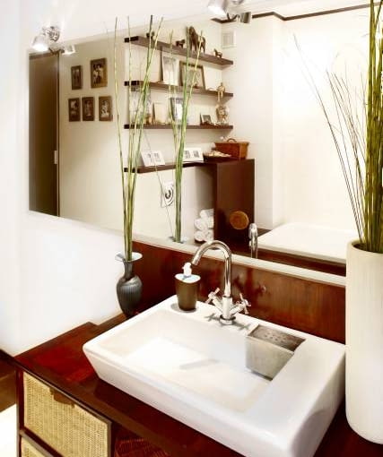 Ciemny brąz umeblowania efektownie kontrastuje z jasnymi płytkami ceramicznymi położonymi na ścianach i na podłodze. Pod umywalką umieszczono kosze-szuflady na niezbędne łazienkowe akcesoria oraz okrągły kosz na brudną bieliznę.