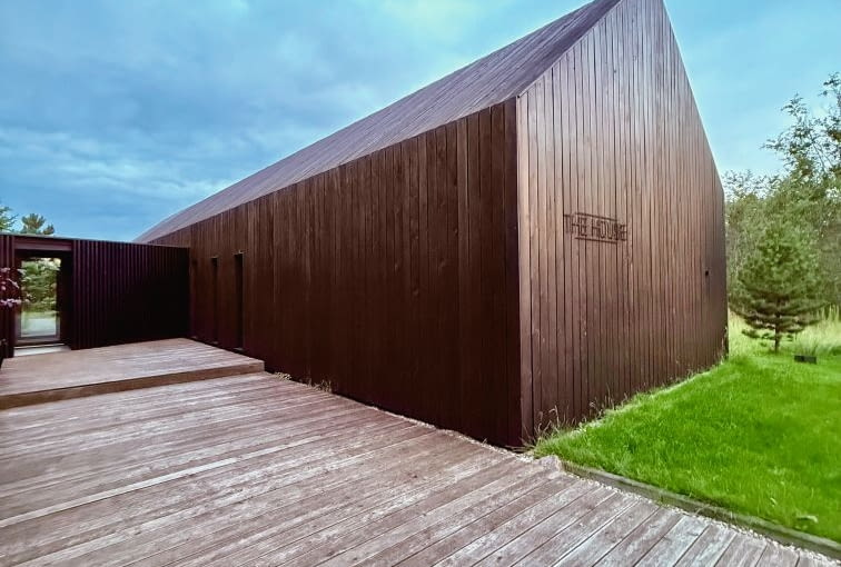 Widok od wjazdu na działkę i garażu, w stronę wejścia głównego. Wiedzie tu trakt komunikacyjny z desek, który przenika przez łącznik i zmienia się po drugiej stronie w taras wypoczynkowy Widok od wjazdu na działkę i garażu, w stronę wejścia głównego. Wiedzie tu trakt komunikacyjny z desek, który przenika przez łącznik i zmienia się po drugiej stronie w taras wypoczynkowy