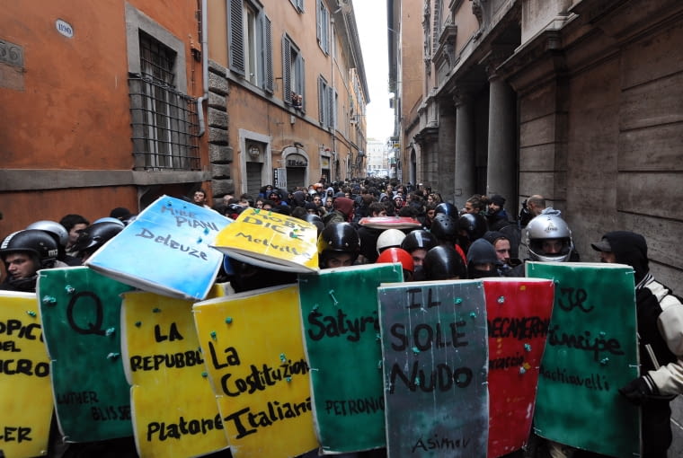 Studenci maszerują ulicami Rzymu z tarczami imitującymi okładki podręczników w proteście przeciwko reformom uniwersytetu. Rzym, 2010 Students, holding shields with titles of books written on them, face police in a tiny street downtown Rome on November 24, 2010. Some 2000 students took to the streets to protest a reform of the university system and budget cuts decided by Prime Minister Silvio Berlusconi's government. AFP PHOTO / ALBERTO PIZZOLI