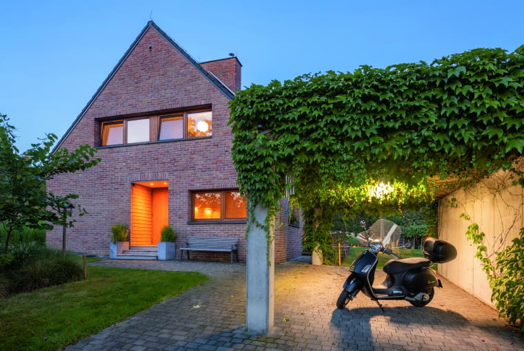 Właściciele i jednocześnie projektanci stoczyli nie lada bój z urzędnikami broniącymi zapisów miejscowego planu zagospodarowania przestrzennego, nakazujących wykonanie tradycyjnych okapów. Na szczęście regulacje dotyczące garażu, widocznego po prawej, nie były już tak restrykcyjne i pozwalały na wzniesienie dość dowolnego betonowego obiektu z dachem płaskim