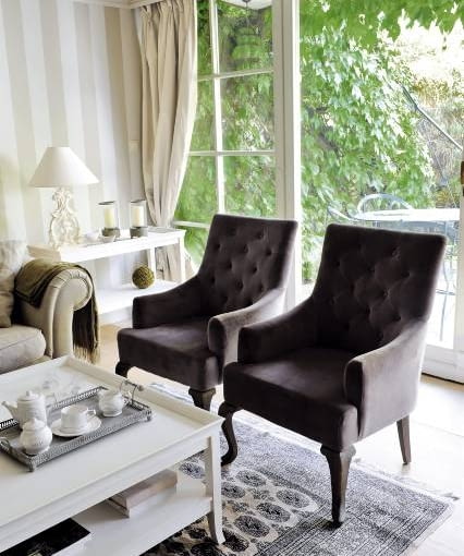 Fotele ludwiki, obite aksamitem o barwie zszarzałego bakłażana, to jedyny mocniejszy akcent kolorystyczny w tym wnętrzu. W oknie wiszą jasne jedwabne zasłony.