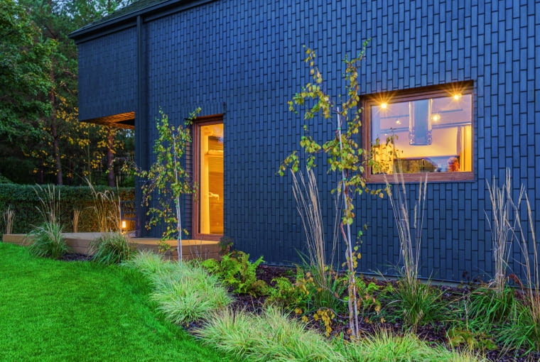 Kolorystykę bryły definiuje nie tylko barwa materiału elewacyjnego, czyli wertykalnie ułożonej cegły klinkierowej, ale także to, co widać za oknami – zwłaszcza o zmierzchu i po zmroku, gdy ciepłe światło z wnętrz świetnie uzupełnia się z czernią ścian ocierającą się o głęboki granat Kolorystykę bryły definiuje nie tylko barwa materiału elewacyjnego, czyli wertykalnie ułożonej cegły klinkierowej, ale także to, co widać za oknami – zwłaszcza o zmierzchu i po zmroku, gdy ciepłe światło z wnętrz świetnie uzupełnia się z czernią ścian ocierającą się o głęboki granat