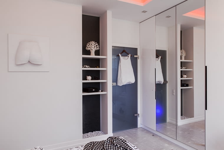 SYPIALNIA. Szklane drzwi zostały zrobione na zamówienie - od strony sypialni ościeżnica jest biała, z zewnątrz - fornirowana drewnem. Obok we wnęce zainstalowano drugą szklaną taflę - w ten sposób doświetlono łazienkę za ścianą (podłogę wnęki dekorują marmurowe kamyki). Środkowa, hartowana część tafli, została specjalnie stłuczona, tak by pęknięcia stanowiły dodatkową ozdobę.