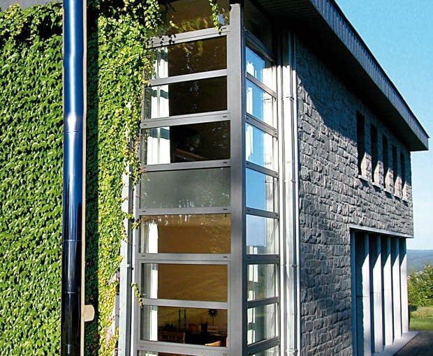 Dym z kominka z płaszczem wodnym można odprowadzić za pomocą dwuściennego komina ze stali, zamontowanego na zewnątrz domu kominek, zielona elewacja, dom nowoczesny