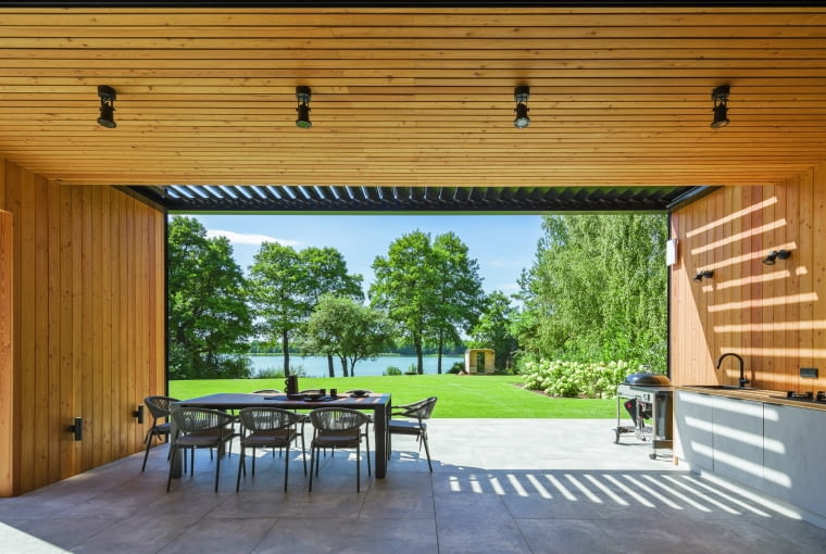 Kilka metrów obok, w ogrodowym tarasie krótszego budynku urządzono strefę letniego salonu, połączoną z kuchnią i grillem. Oba tarasy oczywiście kadrują widoki na jezioro Kilka metrów obok, w ogrodowym tarasie krótszego budynku urządzono strefę letniego salonu, połączoną z kuchnią i grillem. Oba tarasy oczywiście kadrują widoki na jezioro