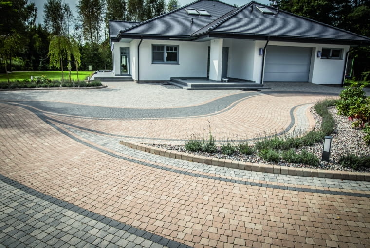 Dobrym wyborem są kostki betonowe w stonowanej kolorystyce (szarości, beże, brązy), nawiązujące do starych bruków, często o nieregularnej fakturze i kształcie