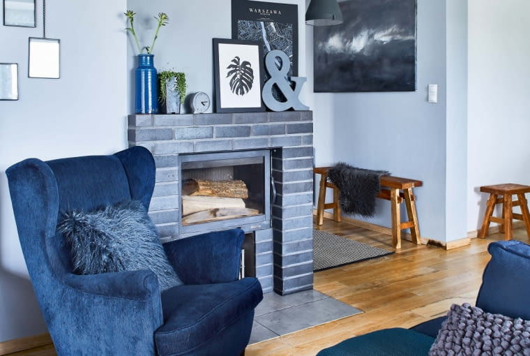 Granat to ulubiony kolor właścicielki. Fotel uszak odziedziczony po dziadkach obiła tkaniną dobraną pod kolor kanapy. Kolor ten z dominującymi w domu grafitami i szarościami tworzy eleganckie trio ocieplone brązem. Obudowa kominka została zrobiona według pomysłu właścicielki z cegły klinkierowej.