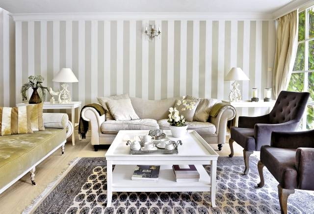 Ścianę pomalowano w szerokie szaro-beżowe pasy (podobny kolor mają obicia niektórych tapicerowanych mebli). Po obu stronach kanapy stoją stoliki pomocnicze; na nich wyeksponowano dekoracyjne przedmioty.