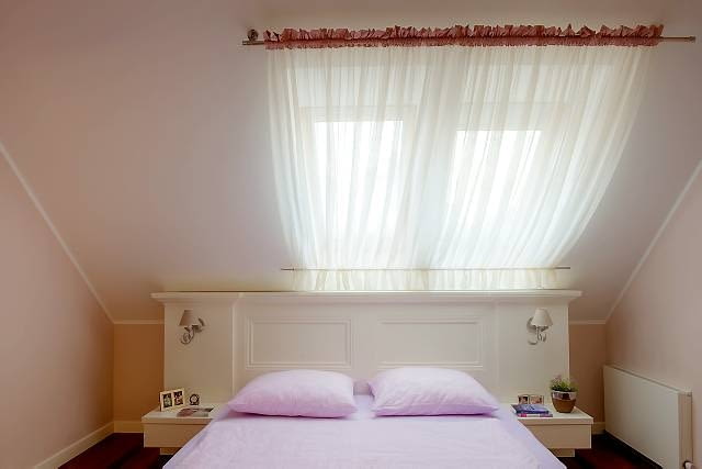 DEKORACJE - NASTROJOWE OKNO NA PODDASZU. Zasłonka z przezroczystego woalu jedynie delikatnie przesłania okno. Do jego szczelnego zasłonięcia służą białe rolety z usztywnionej tkaniny. Pod suto upiętym woalem są niemal niewidoczne.