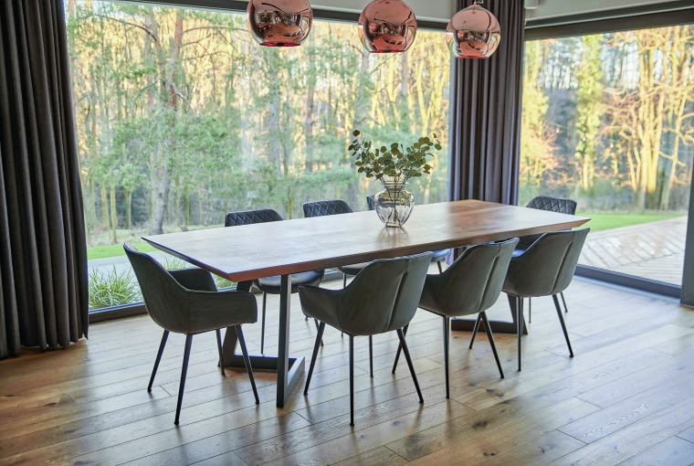 Dębowy stół w jadalni, o wymiarach 290 x 110 cm, robiony był na zamówienie, dzięki czemu nie tylko zaspokaja potrzeby czworga mieszkańców, ale też idealnie wpasowuje się w to miejsce, ukierunkowane widokowo na las