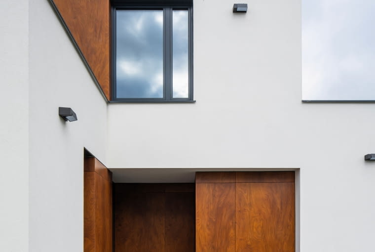 Ponieważ na tej działce stał kiedyś dom z dwoma oddzielnymi lokalami mieszkalnymi, do których szło się z dwóch różnych stron, architekt wykorzystał teraz oba szlaki do podziału na strefę pieszą i dla aut – tu widzimy wejście do budynku dla niezmotoryzowanych... Dom z kostki