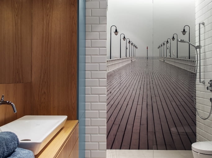 W łazience uwagę przykuwa czarno-białe zdjęcie orłowskiego molo, a także wnęka w wykończeniu z dębowej czeczoty, która pięknie kontrastuje z morską barwą meblowej zabudowy. To w niej chowają się kosmetyki, pralka, deska do prasowania i pozostałe przybory potrzebne do utrzymania porządku. Dzięki temu łazienka jest uporządkowana.