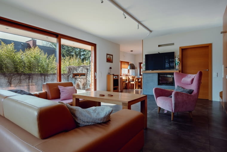 Salon ujęty z drugiej strony, z widokiem na jadalnię i kuchnię, a bliżej na telewizor i usytuowany pod nim kominek. Właścicielom bardzo zależało na obecności kominka i to w centralnej części parteru. Listę życzeń co do wnętrz otwierał jednak... dąb, dużo dębu