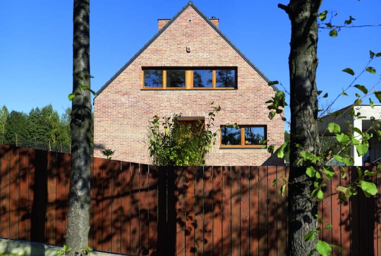 Ceglane elewacje, dwuspadowy dach, prostokątny obrys bryły - powstał bardzo tradycyjny w formie dom, wyglądający trochę jak wyremontowany i solidnie odświeżony o akcenty nowoczesności budynek sprzed stuleci, świetnie wpisany w naturalne otoczenie