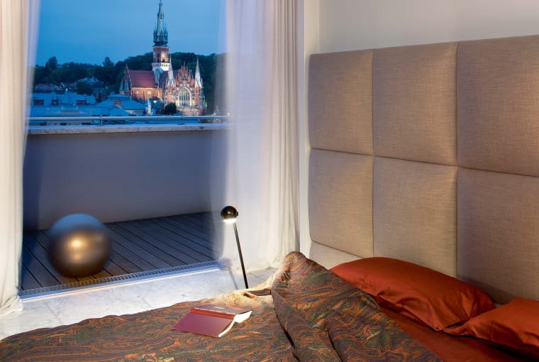 Miejski pejzaż na dobranoc: wieża kościoła św. Józefa wznosząca się nad dachami Podgórza. Łóżko James (Comforty), lampka nocna (Reflex-Studio). Miejski pejzaż na dobranoc: wieża kościoła św. Józefa wznosząca się nad dachami Podgórza. Łóżko James (Comforty), lampka nocna (Reflex-Studio).