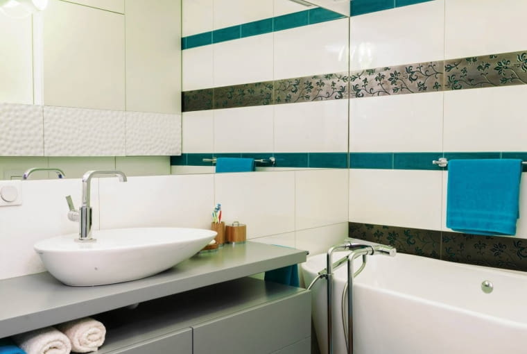 ŁAZIENKA. Szafkę i blat pod umywalkę zrobiono z płyty MDF lakierowanej na jasnoszary odcień. Również tutaj można się dopatrzyć morskich skojarzeń - umywalka przypomina łódkę (wydłużony kształt umożliwia wygodne korzystanie z niewielkiego urządzenia). Kinkiety nad lustrem wtapiają się w tło; wzrok przyciąga natomiast efektowna lampa sufitowa Slamp włoskiej firmy Goccia.