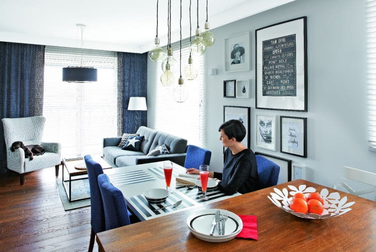 SPORY STÓŁ (ze sklepu Take me Home) z tapicerowanymi krzesłami (domartstyl.eu) przystawiono do wyspy. Ewa i Marek bardzo sobie chwalą to rozwiązanie, bo przygotowując posiłek dla gości, nie czują się wyłączeni z życia towarzyskiego. Ozdobą tej części pomieszczenia jest galeria grafik, zdjęć i plakatów oprawionych w białe i czarne ramki. Nad stołem - siedem lamp-żarówek (bylight.pl).