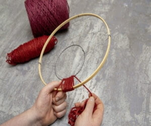 Owiń sznurek w różnych kolorach wokół drewnianej i falistej obręczy, aż obie będą całkowicie pokryte. Zmieniając kolory, tworzysz wzorzysty pierścień o wyglądzie przypominającym tkaninę.