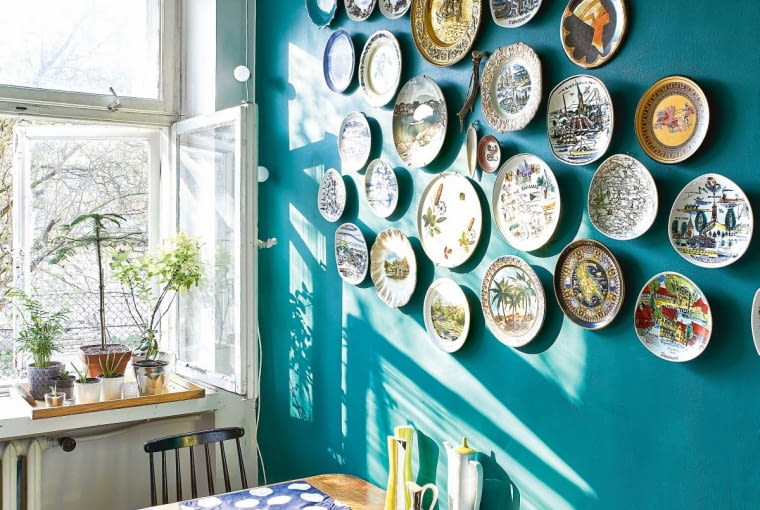 NAD STOLIKIEM ŚNIADANIOWYM kolekcja talerzy wyszperanych na targach staroci. - To talerze z podróży, w których nigdy nie byłam - śmieje się właścicielka. - Ale kiedyś na pewno pojadę w namalowane na nich miejsca. Podkładki w grochy kupiono w Home Sweet Home.