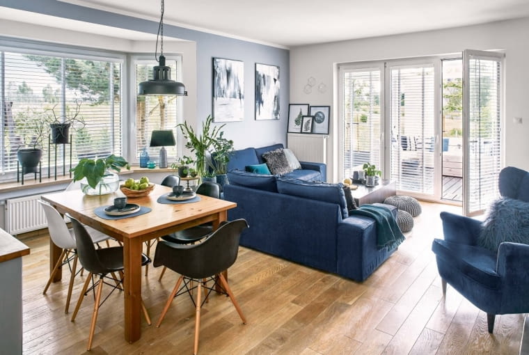 Cztery kolory: granat, szarość, brąz i czerń dominują w całym wnętrzu. Stół i kanapa są z IKEA, talerze - z Malabelle, lampa to Nowodvorski Lighting, włóczkowe pufy - decovena.pl. Świeczniki-kinkiety nad grzejnikiem przyjechały ze sklepu Joanny (artisanhome.pl).