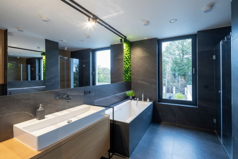 W łazience górnej kondygnacji panuje atmosfera regeneracji psychiki, pielęgnacji ciała i dbałości o zdrowie, podkreślona przez panel gąbczastego mchu. Czy sprzyja temu odwrócenie dominującej w domu kolorystyki przez wprowadzenie ciemnych płytek? Najwyraźniej tak... Dom z kostki