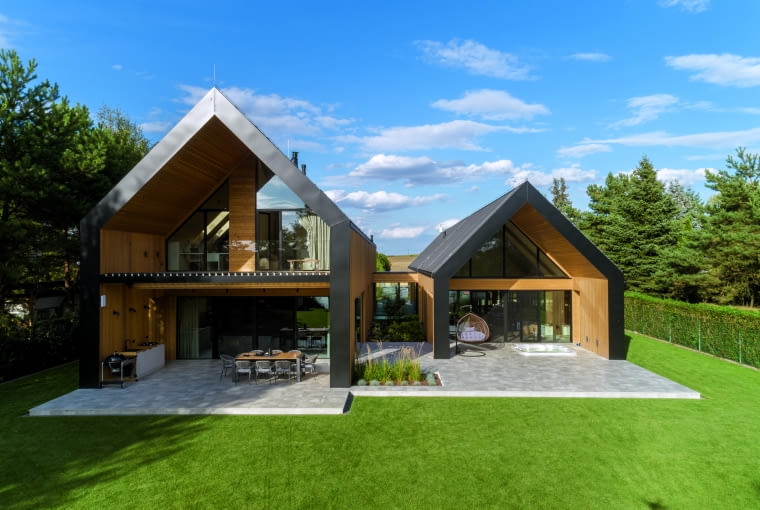 Od strony ogrodu obie bryły nie muszą już niczego zasłaniać i otwierają się na naturę. Drewno połączone z wielkimi przeszkleniami tworzy wrażenie ciepła i przytulności, podczas gdy ciemne dachy i czarne wykończenia wnoszą intrygujący akcent nowoczesności Od strony ogrodu obie bryły nie muszą już niczego zasłaniać i otwierają się na naturę. Drewno połączone z wielkimi przeszkleniami tworzy wrażenie ciepła i przytulności, podczas gdy ciemne dachy i czarne wykończenia wnoszą intrygujący akcent nowoczesności