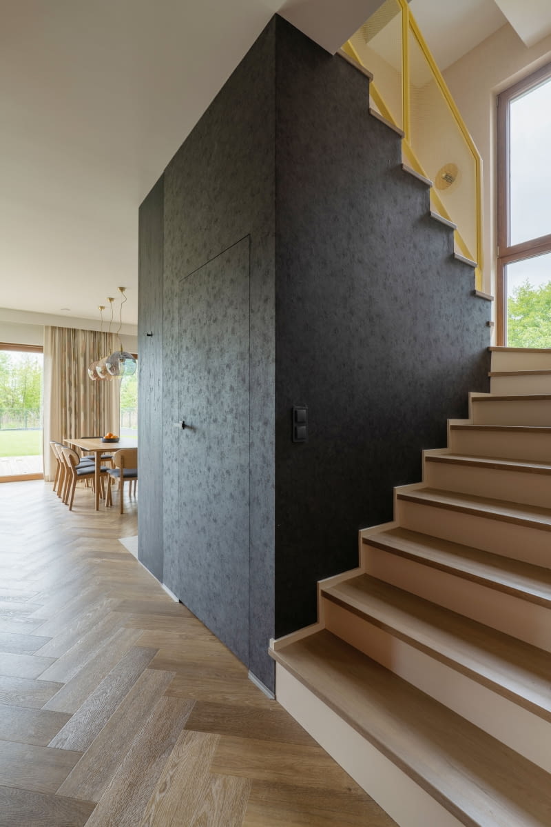 Pod schodami urządzono spiżarnię obsługującą kuchnię. Prowadzą do niej drzwi z ukrytą ościeżnicą, zlicowane ze ścianą i wykończone wspomnianą czarną tapetą Caselio o betonowej strukturze.
