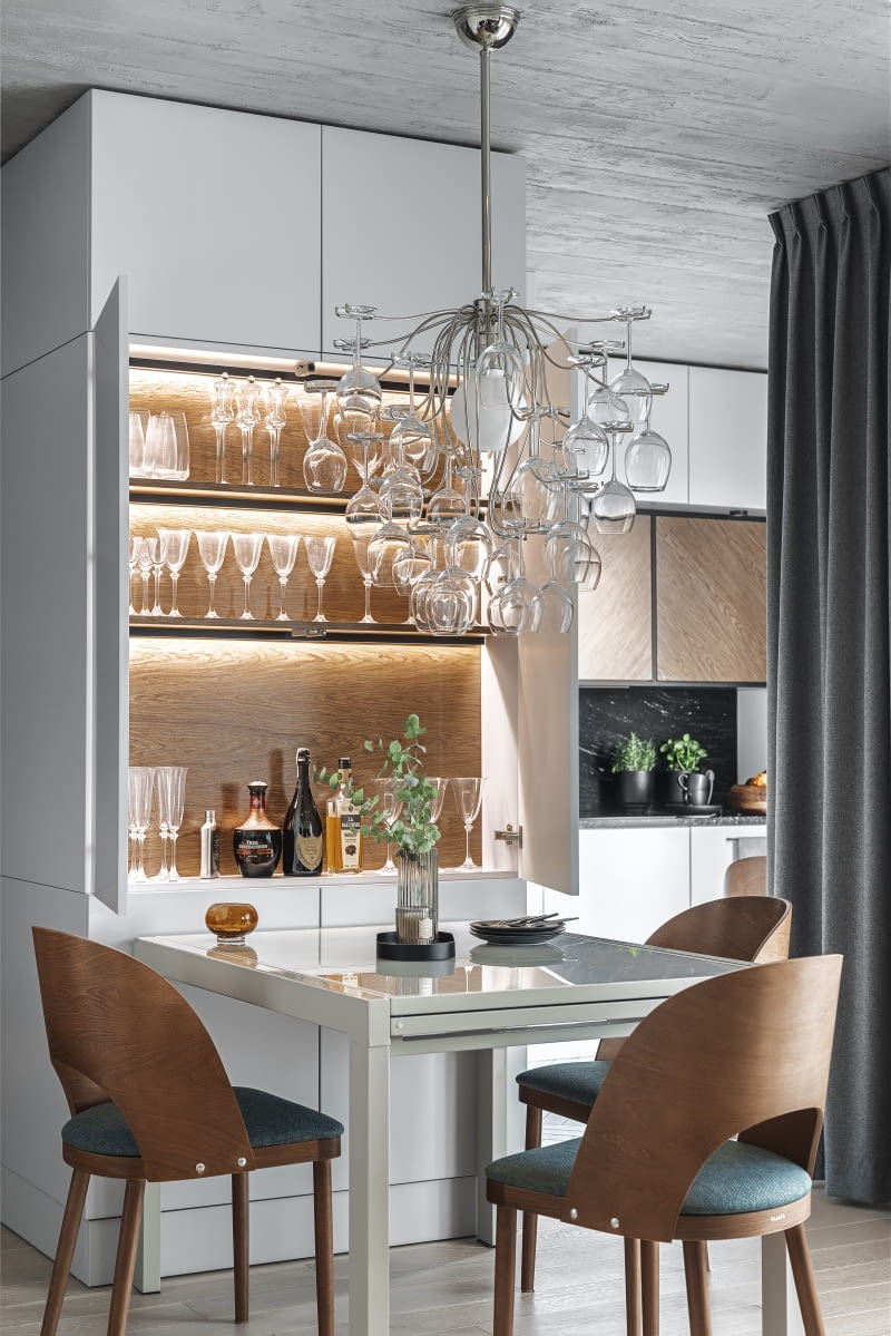 Lampa Sauvignon zawisła nad stołem z sfmeble.pl. Jasnoszary, rozkładany na długość 240 cm mebel wtapia się w zabudowę meblową, przy której stanął. Ozdobą są dobrane do niego krzesła Avola od Famegu. Kubełkowe oparcia wykonano z bukowej sklejki bejcowanej na kolor podobny do rzechowego forniru. Tapicerkę krzeseł powtórzono na salonowym fotelu. Wnętrze zaplanowanego przy stole barku urozmaica orzechowy fornir i oświetlenie LED-owe. Lampa Sauvignon zawisła nad stołem z sfmeble.pl. Jasnoszary, rozkładany na długość 240 cm mebel wtapia się w zabudowę meblową, przy której stanął. Ozdobą są dobrane do niego krzesła Avola od Famegu. Kubełkowe oparcia wykonano z bukowej sklejki bejcowanej na kolor podobny do rzechowego forniru. Tapicerkę krzeseł powtórzono na salonowym fotelu. Wnętrze zaplanowanego przy stole barku urozmaica orzechowy fornir i oświetlenie LED-owe.