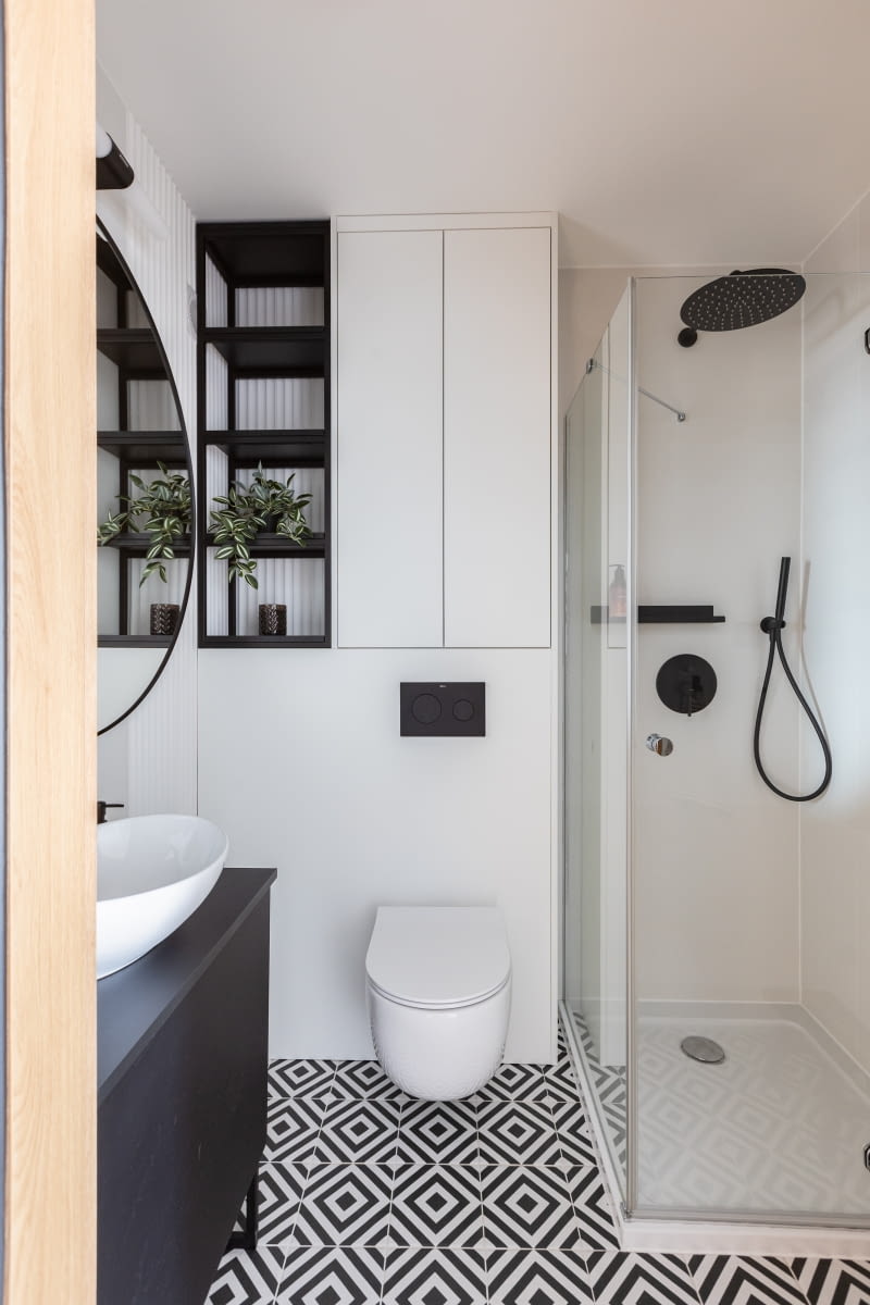 Nieduża kubatura łazienki zdecydowała o wyborze miski WC Meridian marki Roca, która ma mniejsze wymiary niż standardowa toaleta. Również umywalka Etne Oltens jest niewielka, ale jej owalny kształt pozwala na wygodne użytkowanie. Czarny kolor baterii łazienkowych Molle Oltens i przycisku do WC Roca kontrastuje z białym kolorem ścian i zabudowy meblowej. Kabina prysznicowa oraz brodzik – marka Radaway.