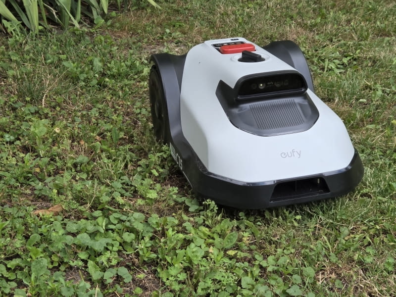 Eufy C15 robot koszący w ogrodzie; widok z przodu, kamera AI i czerwony przycisk STOP Eufy C15 robot koszący w ogrodzie; widok z przodu, kamera AI i czerwony przycisk STOP