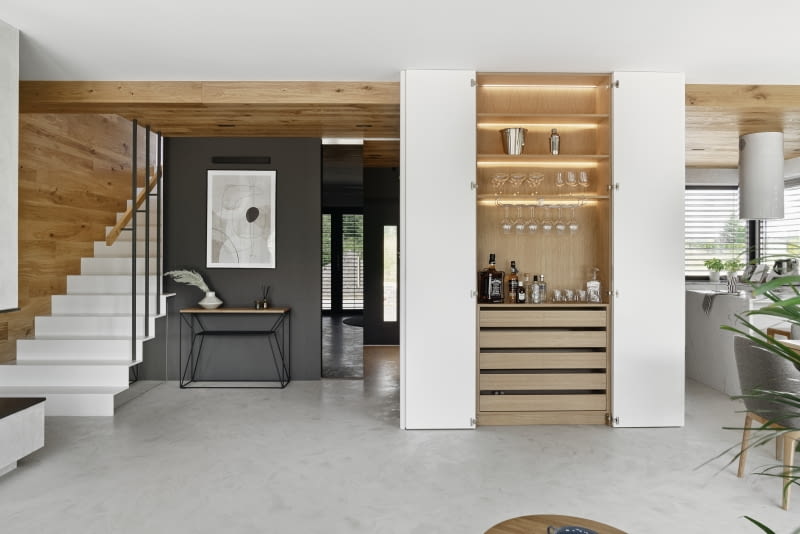 Grafitowa, widziana od strony salonu ściana wiatrołapu, przy której stanęła minimalistyczna konsola od Take me home, płynnie przechodzi w zabudowę kuchenną ze sprzętem AGD w pobliskiej kuchni.