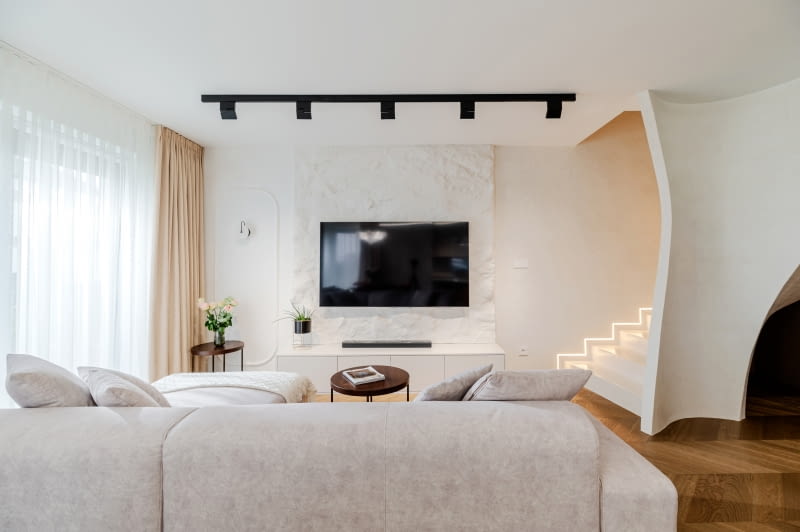 Jeśli w salonie pojawiają się większe zabudowy, np. schody, warto wtopić je w tło, by nie konkurowały z funkcjami.