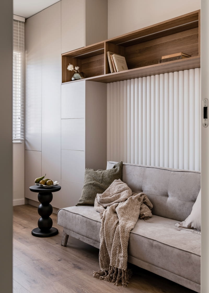 Domowe biuro w razie potrzeby można zmienić w pokój gościnny – rolę łóżka przejmuje wtedy rozkładana sofa Modes  z Customform.  We wnętrzu powtórzono materiały z salonu: białe  lamele, beżowe płyty Egger Kaszmir, z których powstała płytka szafa na dokumenty oraz dekor  Egger Curneo Brązowy wykorzystany do wyko-nania poziomej półki