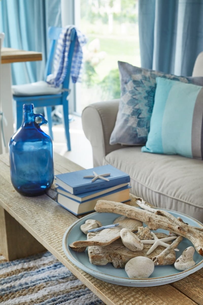 Jasne, rozbielone wnętrze zwieńczone barwą i fakturą naturalnego drewna oraz muśnięte czernią to idealna baza dla kolorystycznych akcentów. Latem w domu króluje błękit w odcieniu bezchmurnego nieba. Towarzyszą mu dodatki i wakacyjne pamiątki nawiązujące do stylizowanego na naturalny, niemal rustykalny wystrój wnętrza.