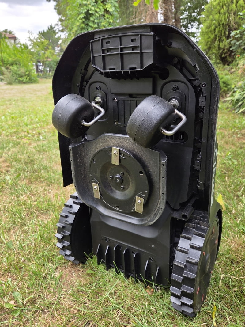 Spód robota: talerz tnący z trzema nożami, dwa kółka podporowe i napędowe koła terenowe. Wszystko łatwo dostępne do czyszczenia. Eufy C15 — spód robota, talerz tnący i koła. Spód robota: talerz tnący z trzema nożami, dwa kółka podporowe i napędowe koła terenowe. Wszystko łatwo dostępne do czyszczenia.