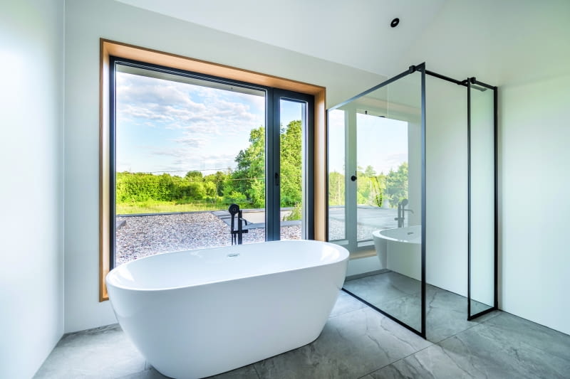 Nie ma dobrej sypialni bez porządnej łazienki. Tuż za ścianą pomieszczenia z łóżkiem właścicieli  znajdują się więc nowoczesna, wolno stojąca wanna oraz prosta do granic możliwości kabina  prysznicowa. Na podłodze – płytki ceramiczne Imola Muse Grey włoskiej firmy Imola Ceramica