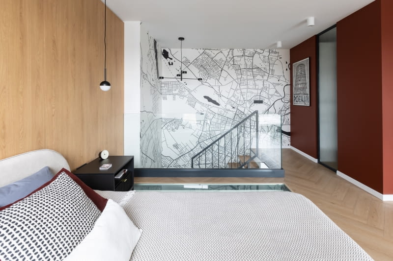 Koncepcja wykończenia ścian sypialni opiera się na wyrazistych płaszczyznach pokrytych wspomnianą tapetą z mapą Poznania, dalej bordową farbą na ścianach garderoby oraz dekoracyjnymi panelami za zagłówkiem łóżka. Płaszczyzny tworzą tło dla dużej, otwartej przestrzeni utrzymanej w podobnym co na parterze reżimie stylistycznym, z niewielką liczbą mebli i dekoracji. Ozdobą jasnego pomieszczenia są detale w czerni i antracycie.