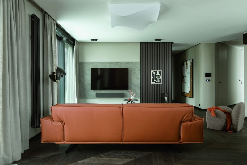 Ściana telewizyjna łączy płyty spieku kwarcowego Cosentino o wyglądzie jasnego kamienia z grafitowymi, lamelowymi panelami PIU Design. W kąciku wypoczynkowym, tuż obok sofy, stolików kawowych i fotela Nobonobo, pojawia się lampa podłogowa Gubi. Aranżację spaja jasnoszary dywan Samarth i szare, w ciepłym tonie zasłony. Całość oświetla biały plafon Axolight. W strefie dziennej uwagę przyciągają też obrazy Ewy Jablonsky rozmieszczone na słupie przy stole i wyspie kuchennej oraz przy korytarzu prowadzącym do części nocnej. Ściana telewizyjna łączy płyty spieku kwarcowego Cosentino o wyglądzie jasnego kamienia z grafitowymi, lamelowymi panelami PIU Design. W kąciku wypoczynkowym, tuż obok sofy, stolików kawowych i fotela Nobonobo, pojawia się lampa podłogowa Gubi. Aranżację spaja jasnoszary dywan Samarth i szare, w ciepłym tonie zasłony. Całość oświetla biały plafon Axolight. W strefie dziennej uwagę przyciągają też obrazy Ewy Jablonsky rozmieszczone na słupie przy stole i wyspie kuchennej oraz przy korytarzu prowadzącym do części nocnej.