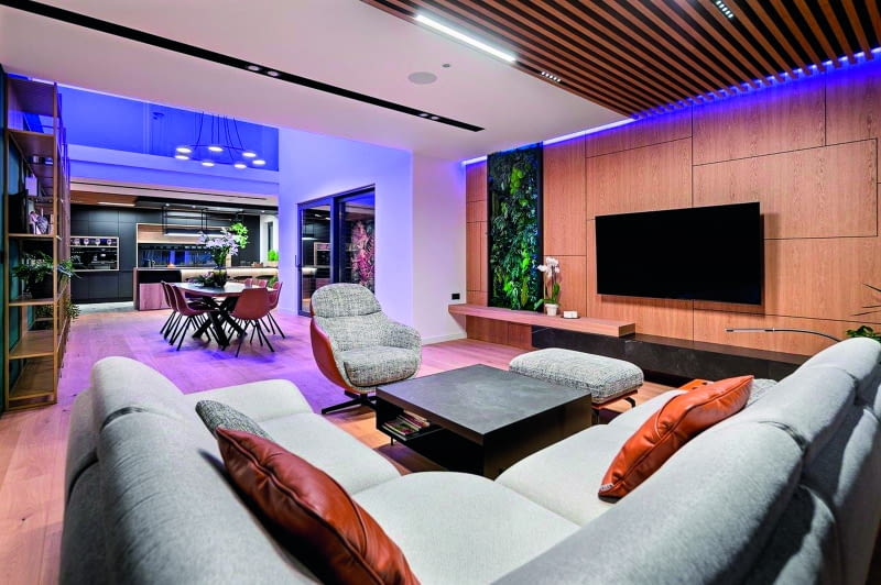 Z tego ujęcia dobrze widać  całą otwartą przestrzeń mieszkalno-gościnną strefy dziennej parteru – wzdłuż jednej  osi zorganizowano, kolejno, wygodny salon,  jadalnię, czyli obszerny stół dla 8-10 osób,  i kuchnię. Poprzez usunięcie sufitu znad jadalni wszystko to otwarto także na piętro