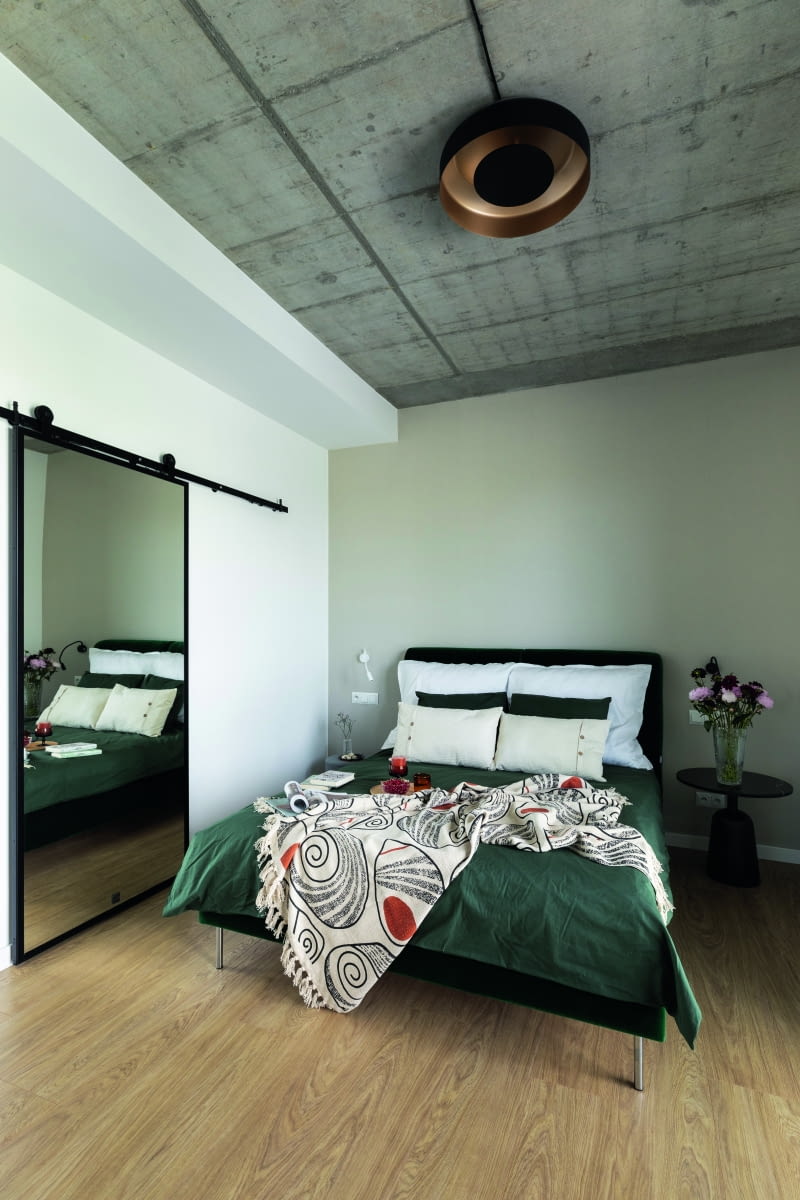 Sypialnia właścicieli, czyli miks klimatów przemysłowo-magazynowych (znowu beton i znowu  intrygująca lampa) oraz wypoczynkowych – lustro, ukrywające przejście do garderoby, jest  jednocześnie lekko rustykalne i orientalne, na podobieństwo azjatyckich przesuwnych przesłon