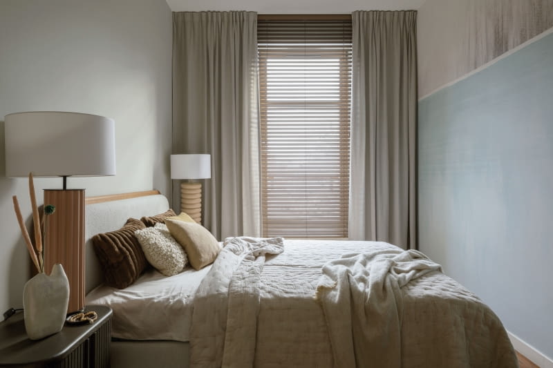 Przyjemna aranżacja wąskiej sypialni odwraca uwagę od trudno ustawnej przestrzeni. Pełnowymiarowe łóżko z NAP z tapicerowanym zagłówkiem pozwala na komfortowy odpoczynek. Ważne są jasne barwy aranżacji,  w tym kolory ścian  i tekstyliów: narzuty, poduszek oraz zasłon.