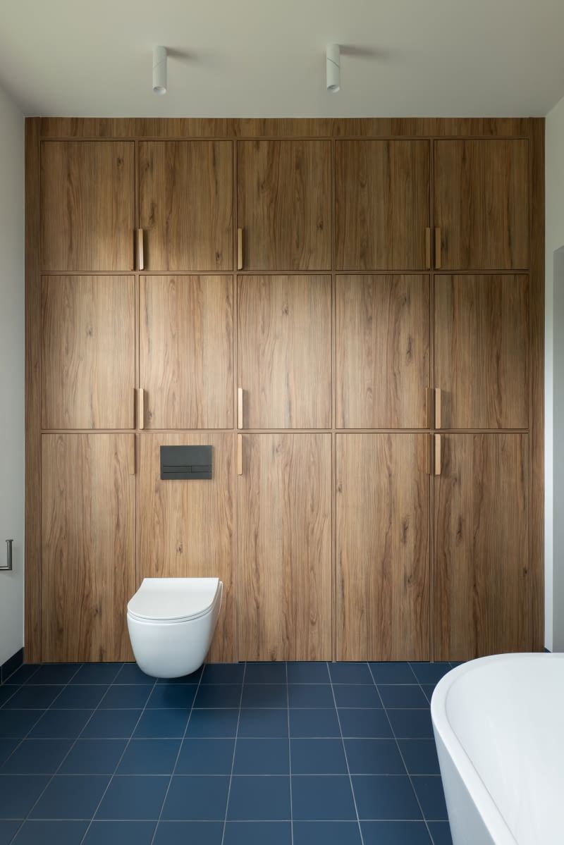 Jedne z drzwiczek zabudowy wokół stelaża WC w łazience dzieci kryją specjalnie wykonany przez stolarza zrzut na ubrania. Po ich otwarciu widać ukryty za nimi kanał, którym odzież trafia bezpośrednio do pralni, do pojemnika na brudne rzeczy po drugiej stronie ściany.