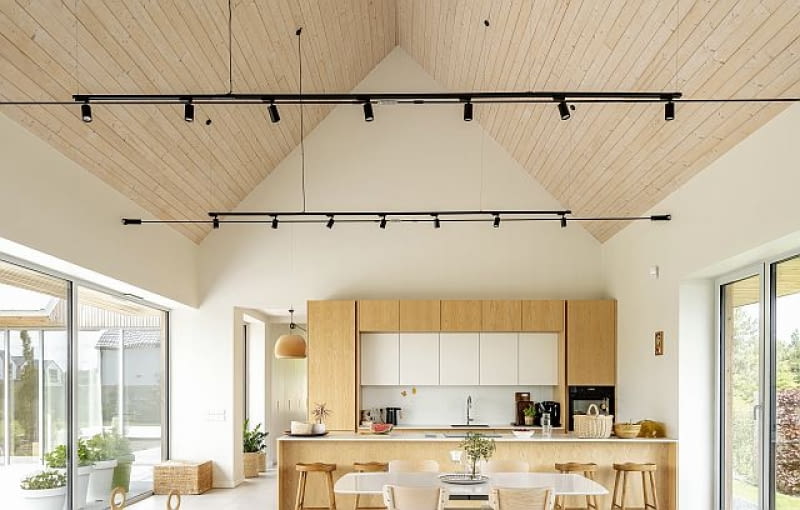 Otwarcie części dziennej na widok podbitych drewnem połaci dachowych powiększa ją, urozmaica wizualnie i zwiększa siłę działania jasnych kolorystycznie materiałów, których tu, podobnie jak na elewacjach, nie brakuje