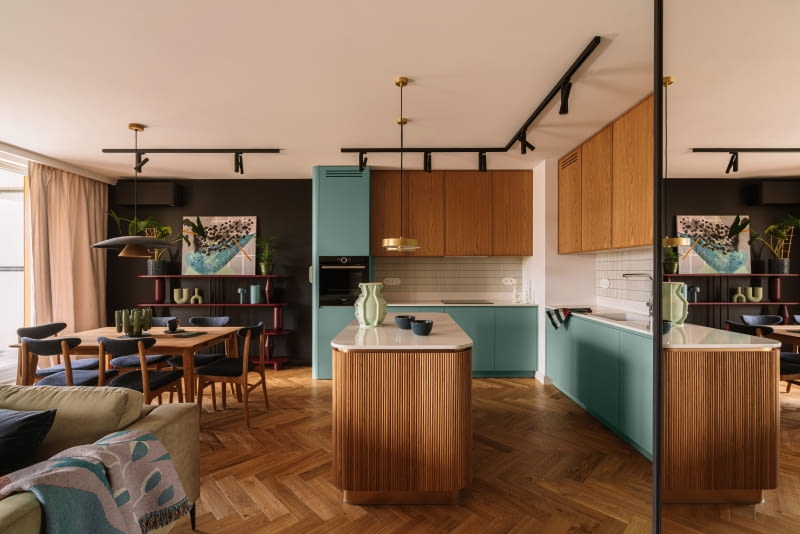 W otwartej części dziennej kuchnia z wyspą, jadalnia i salon przenikają się, tworząc harmonijną przestrzeń, w której kolory  i faktury prowadzą cichą rozmowę.