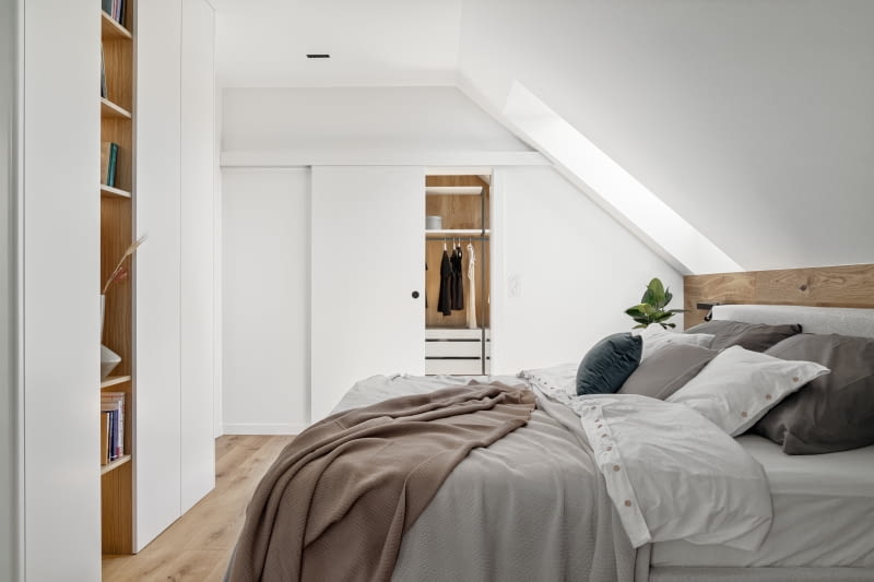 Białe zabudowy meblowe umieszczone naprzeciwko łóżka wykonano z lakierowanych płyt MDF. Mają zaokrąglone narożniki i fornirowane dębowe półki. Formą nawiązują do zabudowy meblowej w jadalni i kuchni. Z podobnych materiałów – białych i fornirowanych płyt – powstało wyposażenie garderoby rodziców, do której przechodzi się bezpośrednio z sypialni.