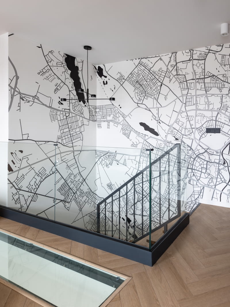 Pomiędzy piętrami, w suficie, nad aneksem kuchennym deweloper przewidział otwór. Ciekawy detal architektoniczny zyskał oprawę ze szkła w antracytowej, podobnie jak konstrukcja i balustrada schodów, stalowej ramie. Przeszklenie doświetla kuchnię i dodaje dodatkowej lekkości całej przestrzeni.