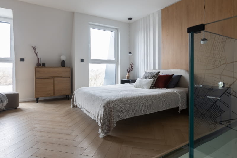 Koncepcja wykończenia ścian sypialni opiera się na wyrazistych płaszczyznach pokrytych wspomnianą tapetą z mapą Poznania, dalej bordową farbą na ścianach garderoby oraz dekoracyjnymi panelami za zagłówkiem łóżka. Płaszczyzny tworzą tło dla dużej, otwartej przestrzeni utrzymanej w podobnym co na parterze reżimie stylistycznym, z niewielką liczbą mebli i dekoracji. Ozdobą jasnego pomieszczenia są detale w czerni i antracycie.