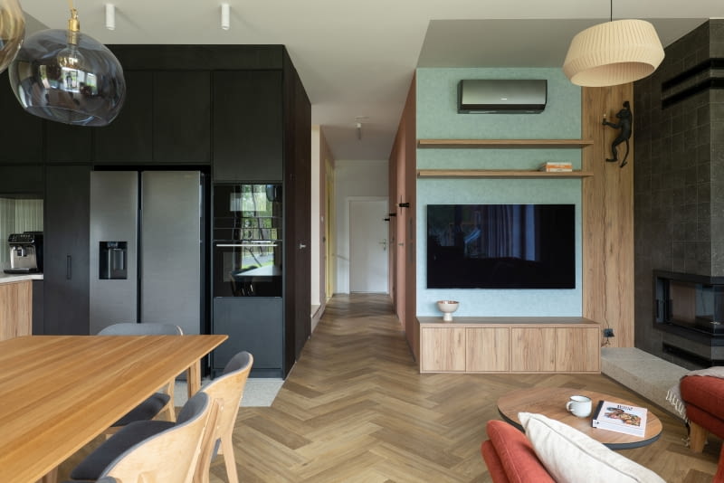 Przy kominku zawieszono lampę małpkę, którą właściciele koniecznie chcieli przemycić do projektu. Architektka od początku uwzględniła ją w koncepcji, projektując układ salonu tak, aby ten charakterystyczny element wyposażenia został harmonijnie wkomponowany w przestrzeń.