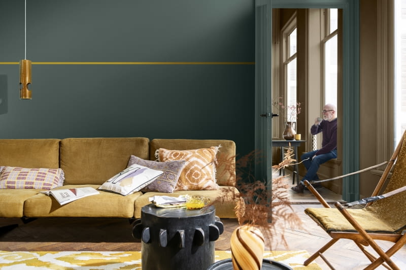 Ciemne barwy tworzą wspaniałą scenerię dla jaśniejszych mebli. Przecinająca ścianę cienka, pozioma linia w odcieniu sofy wprowadzi kolorystyczną równowagę.