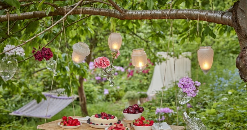 Pomysł na dekorację ogrodowego stołu – szklane lampiony i pelargonie w wazonach.